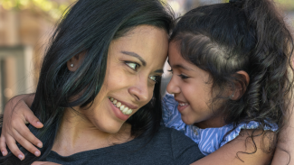 A mom and daughter smile and lean into each other for a tender moment. 